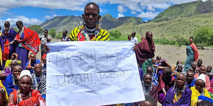 A Maasai women holding a sign saying “This is our ancestral land.” Source: The Maasai Elders, NCA